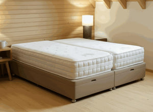 Beige end-lift ottoman bed base with two white mattresses in a rustic room.